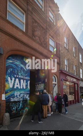 London Shoreditch, Großbritannien. 30. April 2022. Blick auf die Straße vor dem Eingangstor mit Personen, die Van Gogh die Ausstellung „Immersive Experience“ betreten. Stockfoto