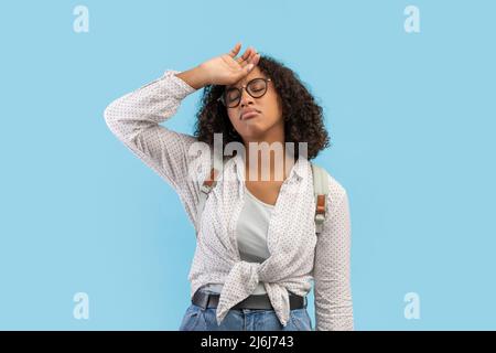 Erschöpfte junge schwarze Studentin mit Rucksack, die sich müde fühlt, sich für die Prüfung bereit zu machen und die Stirn zu wischen Stockfoto