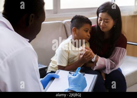 Familienpsychologin. asiatische Mutter und ihr Junge sprechen während der Therapiestunde im Krankenhaus mit dem afroamerikanischen Psychotherapeuten-Arzt. Stockfoto