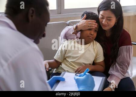 Familienpsychologin. asiatische Mutter und ihr Junge sprechen während der Therapiestunde im Krankenhaus mit dem afroamerikanischen Psychotherapeuten-Arzt. Stockfoto