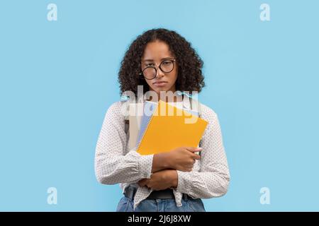 Traurige schwarze Studentin fühlt sich müde und hält Notizbücher auf blauem Studiohintergrund Stockfoto