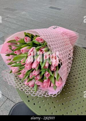 Schöner Frühlingsstrauß von rosa Tulpenin rosa Verpackung, die auf dem Kaffeetisch liegt. Stockfoto