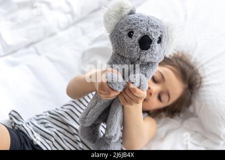 Glückliches kleines Mädchen mit weichem Spielzeug Koala im Bett. Stockfoto