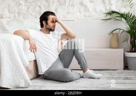 Mürrischer Millennial-Mann, der sich unten fühlt, Schlafzimmer innen Stockfoto