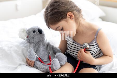 Glückliches kleines Mädchen mit weichem Spielzeug Koala im Bett. Stockfoto