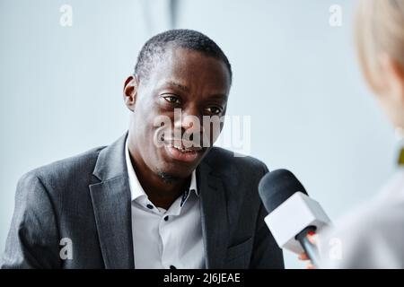Porträt eines erfolgreichen schwarzen Geschäftsmannes, der mit dem Mikrofon spricht und dabei interivew gibt Stockfoto