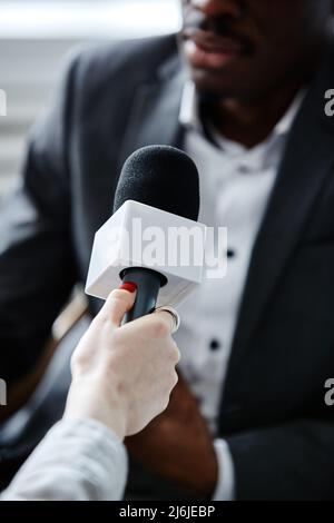 Vertikale Nahaufnahme einer jungen Frau, die das Mikrofon hält, während sie einen Experten interviewt Stockfoto