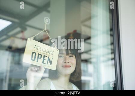 Glücklicher nicht-binärer Geschäftsinhaber, der sein Geschäft wiedereröffnet. Stockfoto