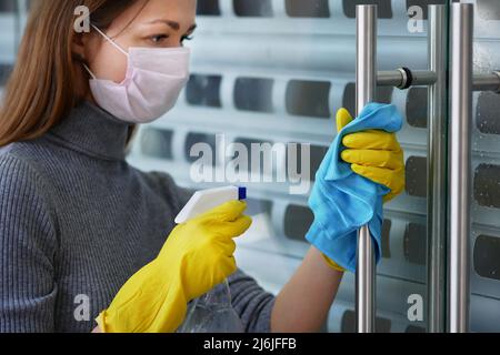 Putzfrau, in Schutzmaske und Handschuhen, wischt Türgriffe mit Antiseptikum im Restaurant oder öffentlichen Einrichtungen. Schutz covid-19 Stockfoto