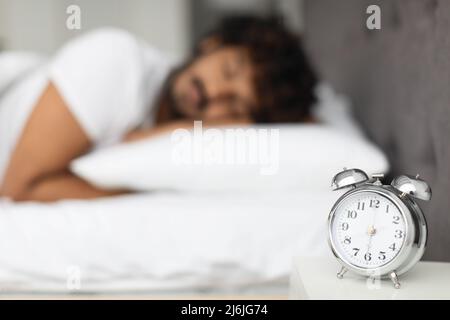 Selektiver Fokus auf Alarm am Bett über schlafenden Mann Stockfoto
