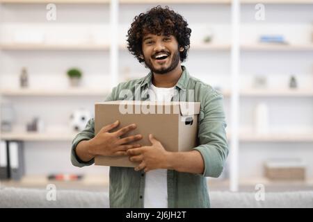 Glücklicher junger indischer Mann umarmt Box zu Hause Stockfoto