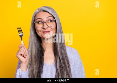 Porträt von charmanten liebenswert verhungernden Großmutter wählen Gericht aus dem Menü isoliert auf gelbem Hintergrund Stockfoto