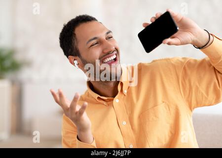 Aufgeregter arabischer Mann, der mit dem Handy Kopfhörer trug und sang Stockfoto