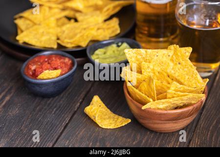 Nachos mit Guacamole, roter Chilisauce und Bier auf Holztisch der berühmteste mexikanische Snack-Hintergrund. Stockfoto