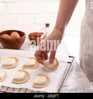 Frau setzte Empanadillas, kleine, füllende Thunfischpasteten in einen Bräter, um Backgebäck im Ofen zu backen. Typischer Snack in lateinamerikanischen Kulturen und Spanien. Natur Stockfoto