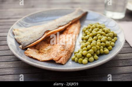 Appetitlich gebackene Forellenfilets mit grünen Erbsen Stockfoto