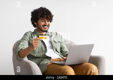 Positiver hindu-Typ mit Laptop und Kreditkarte Stockfoto