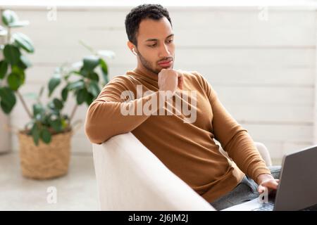 Arabischer Mann mit Laptop, der zu Hause auf der Couch sitzt Stockfoto