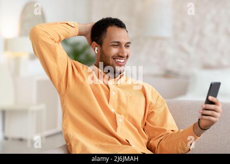 Glücklicher arabischer Mann, der Kopfhörer mit dem Handy trägt Stockfoto