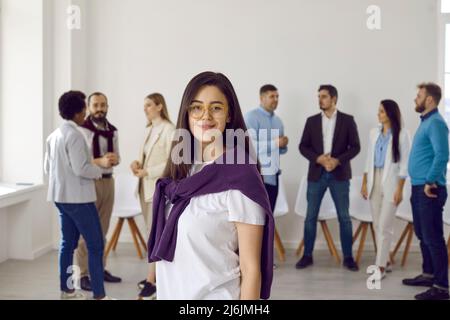 Attraktive Dame in Brillen posiert vor der Kamera im Büro, Geschäftsleute im Hintergrund Stockfoto
