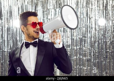 Lustiger junger dunkelhäutiger Mann in Anzug mit Lautsprecher gibt Ankündigung für Valentinstag. Stockfoto