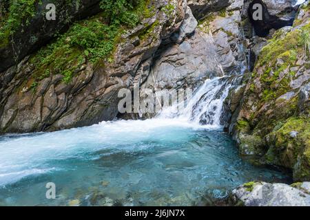 Frisches Wasser aus einem Bergbach fließt über Felsen in einen blau leuchtenden natürlichen Wasserpool. Stockfoto