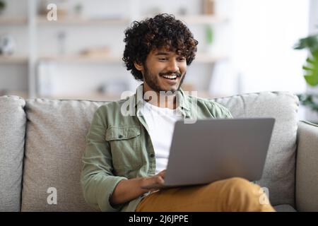Entspannter dunkelhäutig Kerl mit Notebook zu Hause Stockfoto