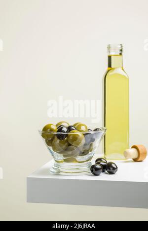 Große grüne und schwarze Oliven in Glasschüssel auf Regal mit Ölflasche Stockfoto