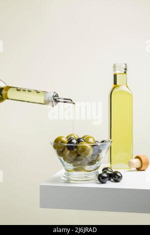 Große grüne und schwarze Oliven in Glasschüssel auf Regal mit Ölflasche Stockfoto