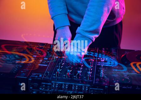 Nahaufnahme bei Neonlicht. Männliche Hände drehen Geräusche auf professionellen dj-Mixer. Gemischter Lichteffekt Stockfoto