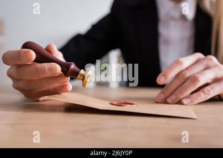 Selektiver Fokus von Staubgefäß und versiegeltem Briefumschlag aus Bastelpapier in den Händen eines beschnittenen Notars auf verschwommenem Hintergrund Stockfoto