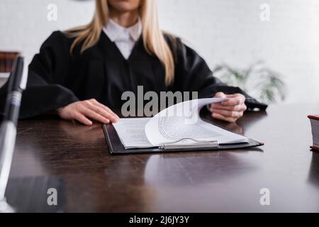 Abgeschnittene Ansicht des Staatsanwalts in schwarzem Mantel, der mit Papieren auf verschwommenem Hintergrund arbeitet Stockfoto