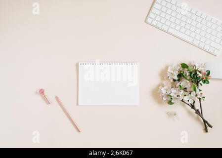 Öffnen Sie das Notizbuch mit einem weißen Blatt Papier, auf dem Sie Platz für Kopien, Tastatur, Stift und weiße Blumen auf einem beigen Hintergrund haben. Flacher Arbeitsbereich Stockfoto