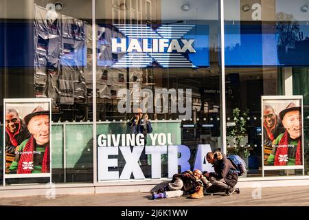 London - April 2022: Halifax High Street Bank Filiale mit einem Obdachlosen auf der Straße draußen Stockfoto