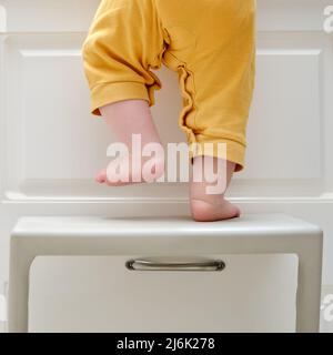 Kleinkind Baby Junge kletterte mit seinen Füßen auf einem Hochstuhl auf den Küchenschrank klettern. Probleme mit der Kindersicherheit im heimischen Zimmer, kleines Kind Stockfoto