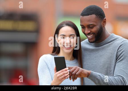 Vorderansicht Porträt eines glücklichen interrassischen Paares, das Telefontext auf der Straße konsultiert Stockfoto