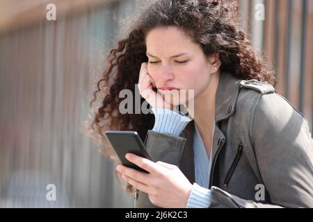 Gelangweilte Frau, die auf der Straße auf dem Smartphone nachgeht Stockfoto