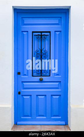 Blaue Holztür mit schwarzem Metallklopfer und weiß getünchte Fassade in Altea, Alicante, Spanien. Stockfoto