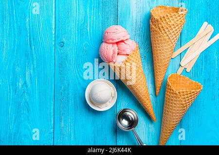 Beeren- und Speiseeis, Waffelbecher und ein Löffel auf blauem Hintergrund. Stockfoto