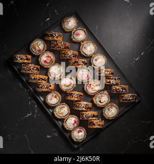 Stellen Sie heiße Sushi-Brötchen auf einem runden Tablett mit köstlichen Tempura und gebackenen Sushi-Maki mit Lachs, Aal, Gurke, Avocado und Rühreiern auf Stockfoto