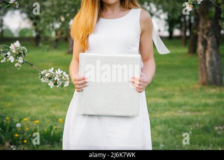 Ein weißes Hochzeitsfotoalbum wird von einer Frau in einem weißen Kleid gehalten Stockfoto