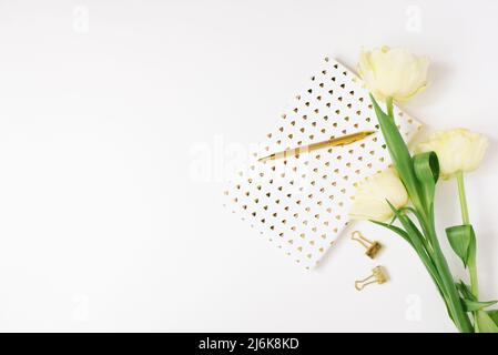 Ein Bouquet aus frühlingsgelben Tulpen, einem Notizbuch auf weißem Hintergrund und einem goldenen Stift. Das Konzept des Frühlings, des Frauen- und Muttertages, des Geburtstages oder des blo Stockfoto