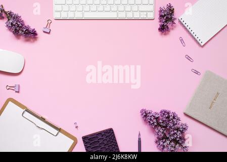 Tastatur und Maus, Notizbücher, Stift, ein Strauß Flieder auf einem rosa Hintergrund. Lila Frühlingsblumen. Komposition für einen Blogger. Speicherplatz kopieren Stockfoto