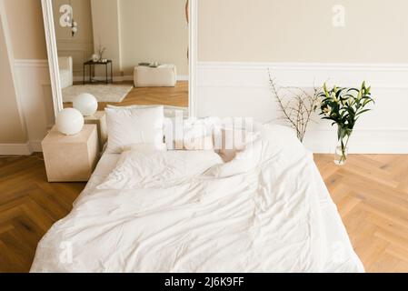 Ein gemütliches Bett auf dem Boden, ein großer Spiegel in einem klassisch-modernen Schlafzimmer. Der Innenraum des Hauses Stockfoto