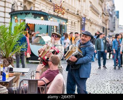 Bukarest, Rumänien - 04.08.2022: Zwei Senioren unterhalten Menschen in einem Restaurant im Freien in der Altstadt mit Akkordeon Stockfoto