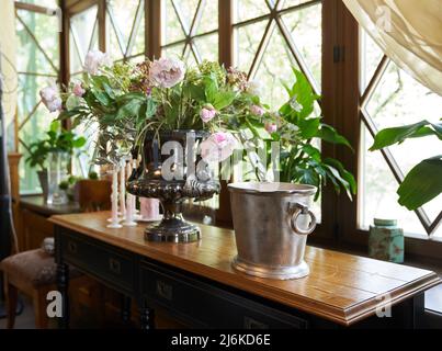 Ein schöner Blumenstrauß von Pfingstrosen bei Tageslicht auf einer hölzernen Fensterbank. Verwelkt rosa Pfingstrosen in einer Vase auf dem Hintergrund des Fensters. Hochwertige Fotos Stockfoto