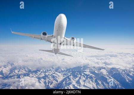 Luftaufnahme Berge aus dem Flugzeug. Fliegen Sie über das schneebedeckte Bergtal bei reinem Sonnenschein mit vorbeiziehenden Wolken Stockfoto