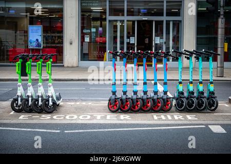 London, April 2022: E-Scooter-Verleih, Motorroller ordentlich aufgereiht in ausgewiesener Bucht. Stockfoto