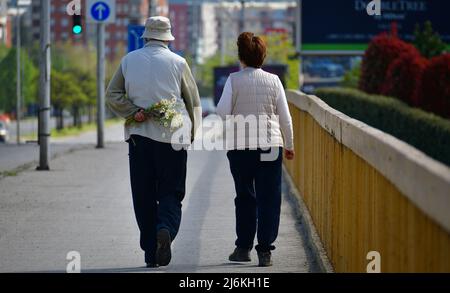 Ein paar alte Leute gehen, einer hält einen Blumenstrauß im Rücken Stockfoto