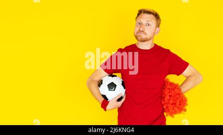 Unglücklicher Fan-Fan, der einen Fußballball auf gelbem Hintergrund hält Stockfoto